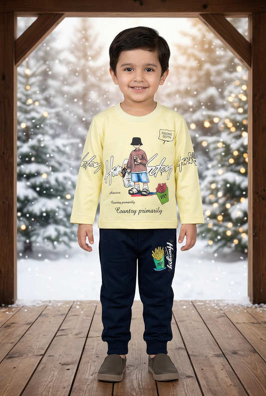 Child wearing BS832 light-yellow character-print Terry top and navy fries-print joggers on a sheltered veranda with snowy pines and warm lights behind.