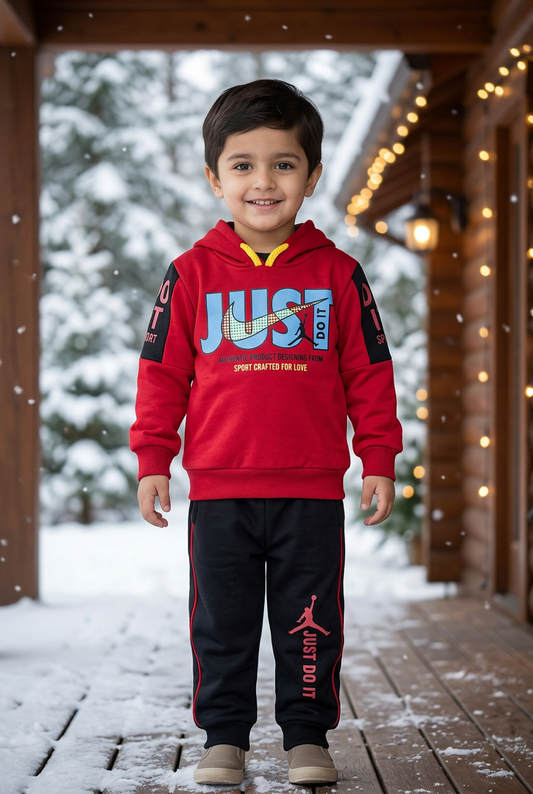 Child wearing BS826 red Terry hoodie with blue lettering and black sleeve panels, and black joggers on a veranda beside snowy pines and warm lights.