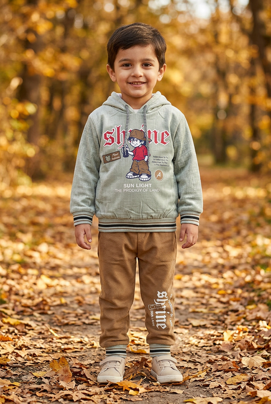 Child wearing BS803 pale sage-green Shine graphic fleece hoodie and brown joggers with striped trims on an autumn park path.