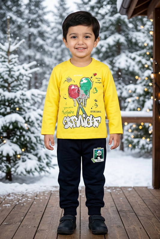 Child wearing BS839 yellow lollipop-print Terry top and dark panda-patch joggers on a sheltered wooden veranda with snowy pines and warm lights behind.