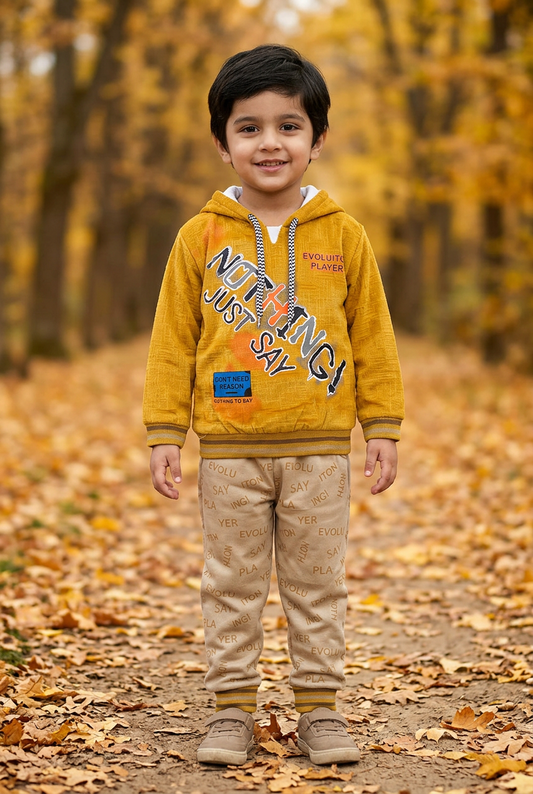 Child wearing BS804 mustard-yellow Nothing graphic fleece hoodie with striped trims and beige lettering-print joggers on an autumn park path.