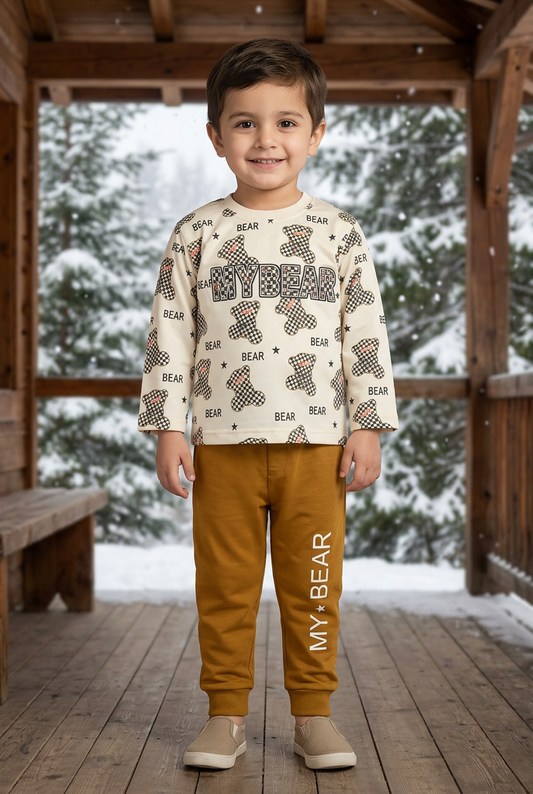 Child wearing BS797 cream checkerboard-bear Terry sweatshirt and mustard MY BEAR joggers on a sheltered wooden veranda with snowy pine trees behind