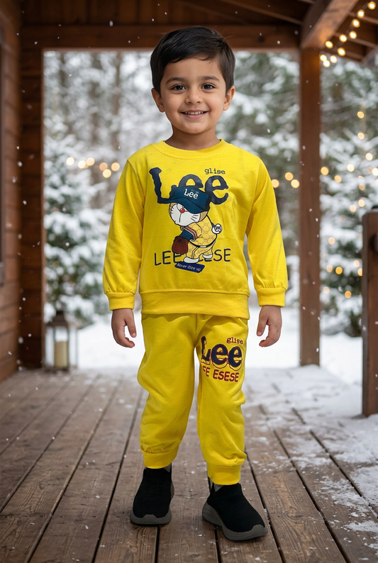 Child wearing BS781 yellow Terry cartoon sweatshirt and matching cuffed joggers on a sheltered wooden veranda with snowy pines and warm lights behind.