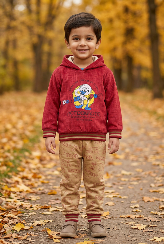 Child wearing BS807 red fleece hoodie with astronaut-duck artwork and beige printed joggers on an autumn park path.
