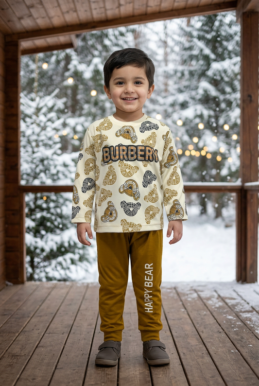 Child wearing BS794 cream bear-head-print Terry top and dark-yellow HAPPY BEAR joggers on a veranda with snowy pines and soft lights behind