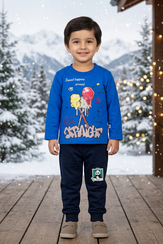 Child wearing BS840 royal-blue lollipop-print Terry top and navy panda-patch joggers on a sheltered veranda with snowy pines and warm lights behind.